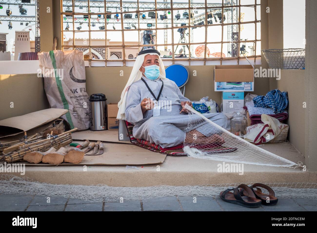 Arabischer Fischer, Reparatur von hausgemachten Fischernetz und Holzyacht, trägt Gesichtsmaske und sitzt auf dem Boden der traditionellen Boam Stockfoto