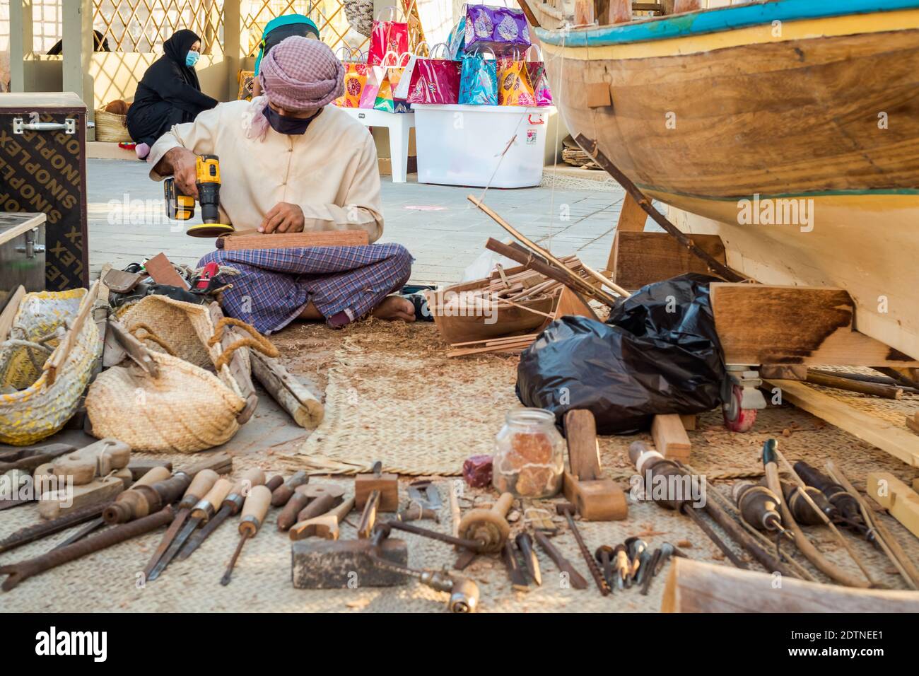 Arabischer Fischer, Reparatur von hausgemachten Fischernetz und Holzyacht, trägt Gesichtsmaske und sitzt auf dem Boden der traditionellen Boam Stockfoto