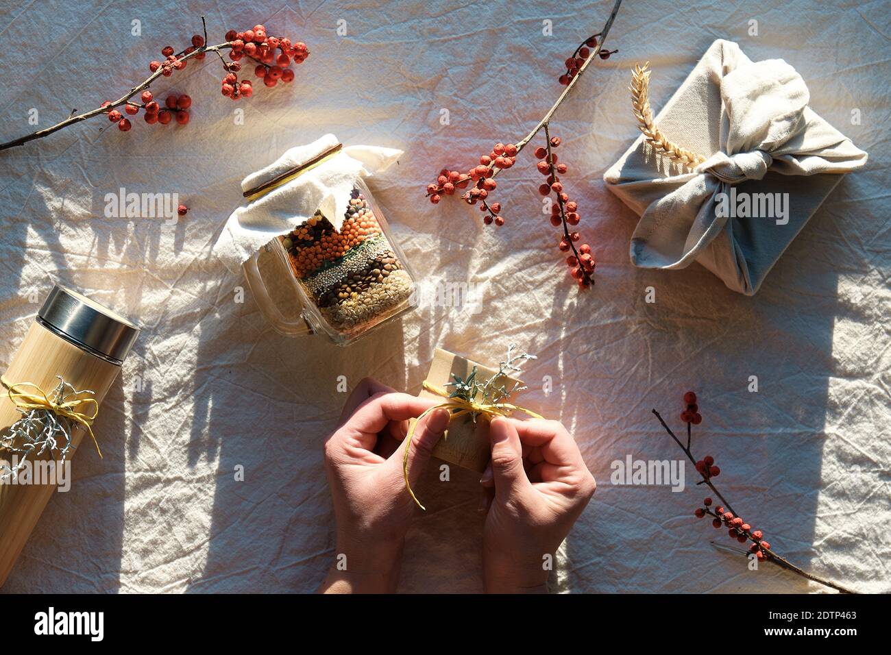 Flat Lay mit Zero Waste Weihnachtsgeschenke. Hände binden Bogen Dekoration Bambus Tasse. Weihnachten Geschenk in Handtuch, Einmachglas mit geschichteten Bohnen verpackt Stockfoto