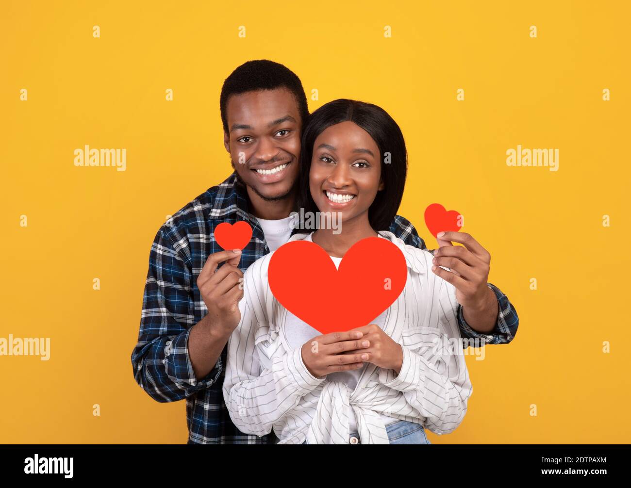 Fröhlicher Urlaub, Romantik, Jubiläum und Liebe. Glücklicher afroamerikanischer Kerl und Dame mit roten Herzen Stockfoto