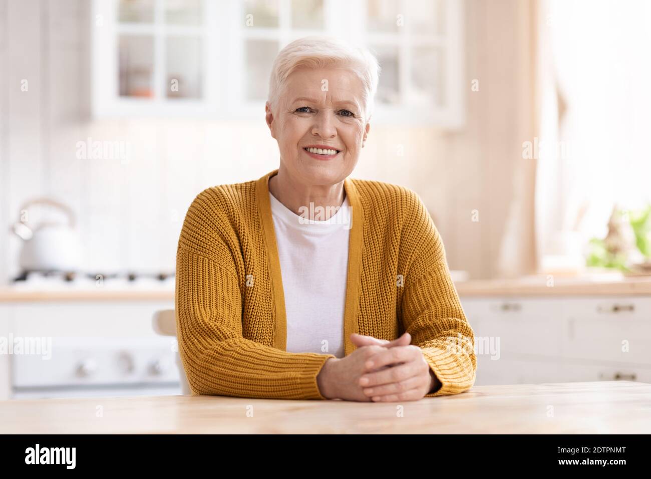 Porträt einer fröhlichen alten Frau, die in der Küche sitzt Stockfoto