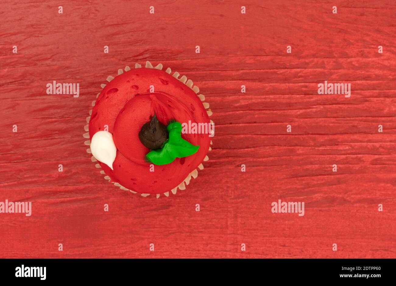 Draufsicht auf einen hell gefrosteten frisch zubereiteten Cupcake auf einem leuchtend roten Hintergrund. Stockfoto