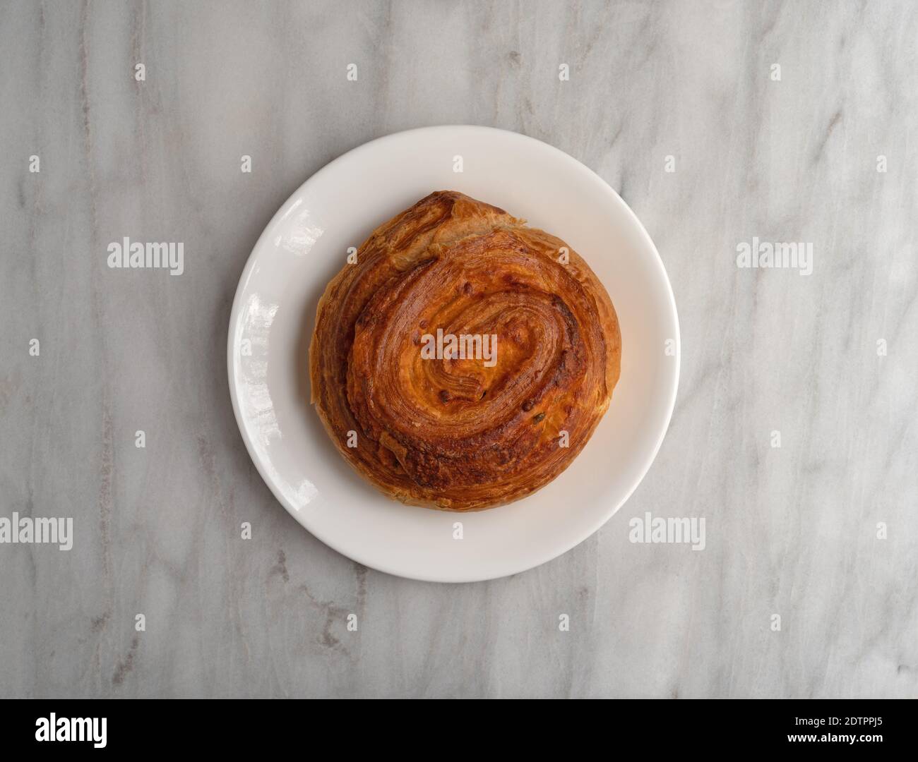 Draufsicht auf ein einzelnes Jalapeno-Käsestrudel-Brot auf einem weißen Teller auf einer grauen Marmorarbeitsfläche, die mit natürlichem Licht beleuchtet ist. Stockfoto