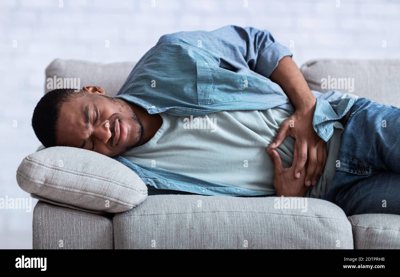 African Guy Leiden An Bauchschmerzen Liegen Auf Sofa Indoor Stockfoto