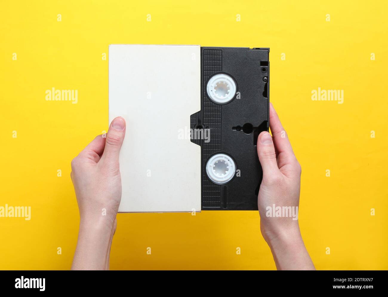 Frau Hände halten Videokassette im Cover, Videoband auf einem gelben Hintergrund.Draufsicht, Minimalismus. Stockfoto