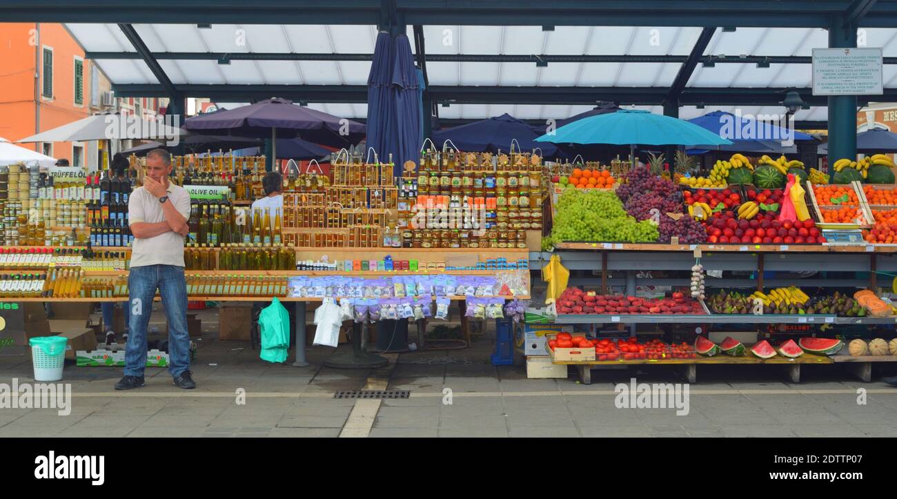Markthändler, der vor Öl-, Kräuter- und Obstständen ohne Kunden steht. Stockfoto