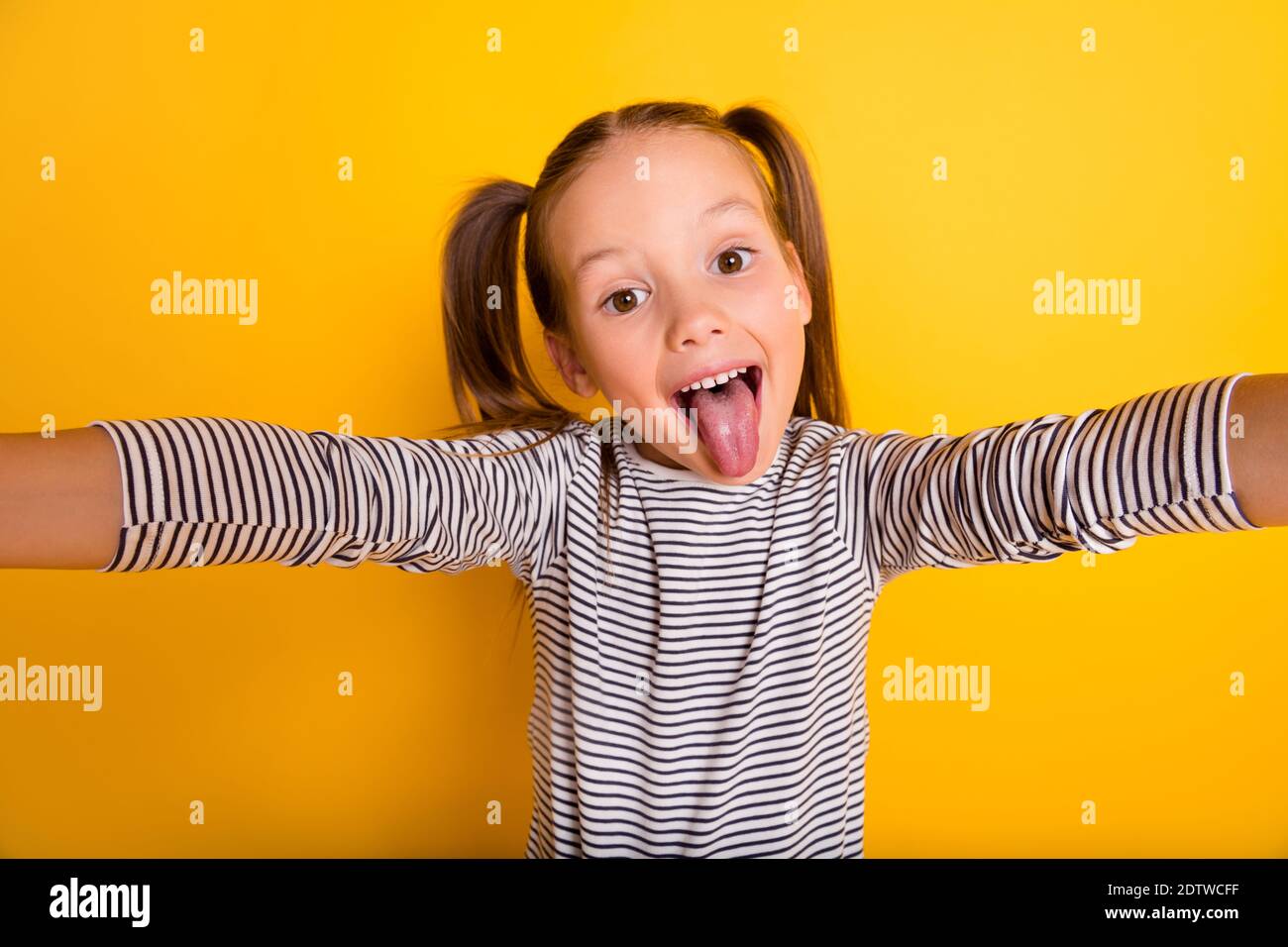 Portrait von jungen funky Narren spielerisch kleines Mädchen Kind Machen Selfie-Stick Zunge aus isoliert auf gelbem Hintergrund Stockfoto