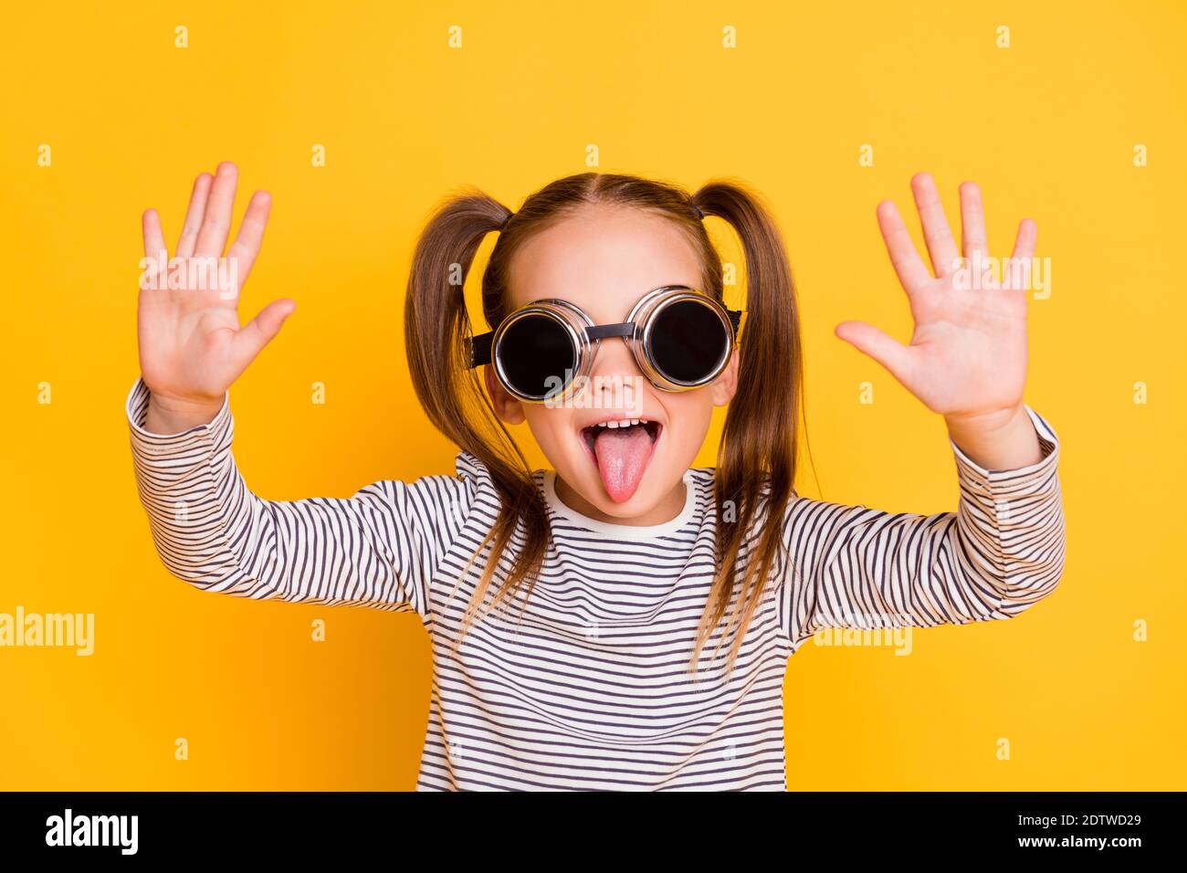 Portrait von jungen Narren humorvoll lächelnd kleines Mädchen Kid Stick Zunge aus tragen funky Sonnenbrille isoliert auf gelbem Hintergrund Stockfoto