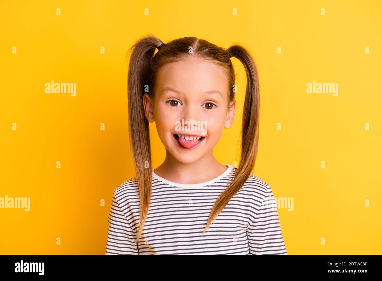 Portrait von jungen lächelnd funky neugierig scherzen Mädchen Kind Kind Stick Zunge isoliert auf gelbem Hintergrund Stockfoto