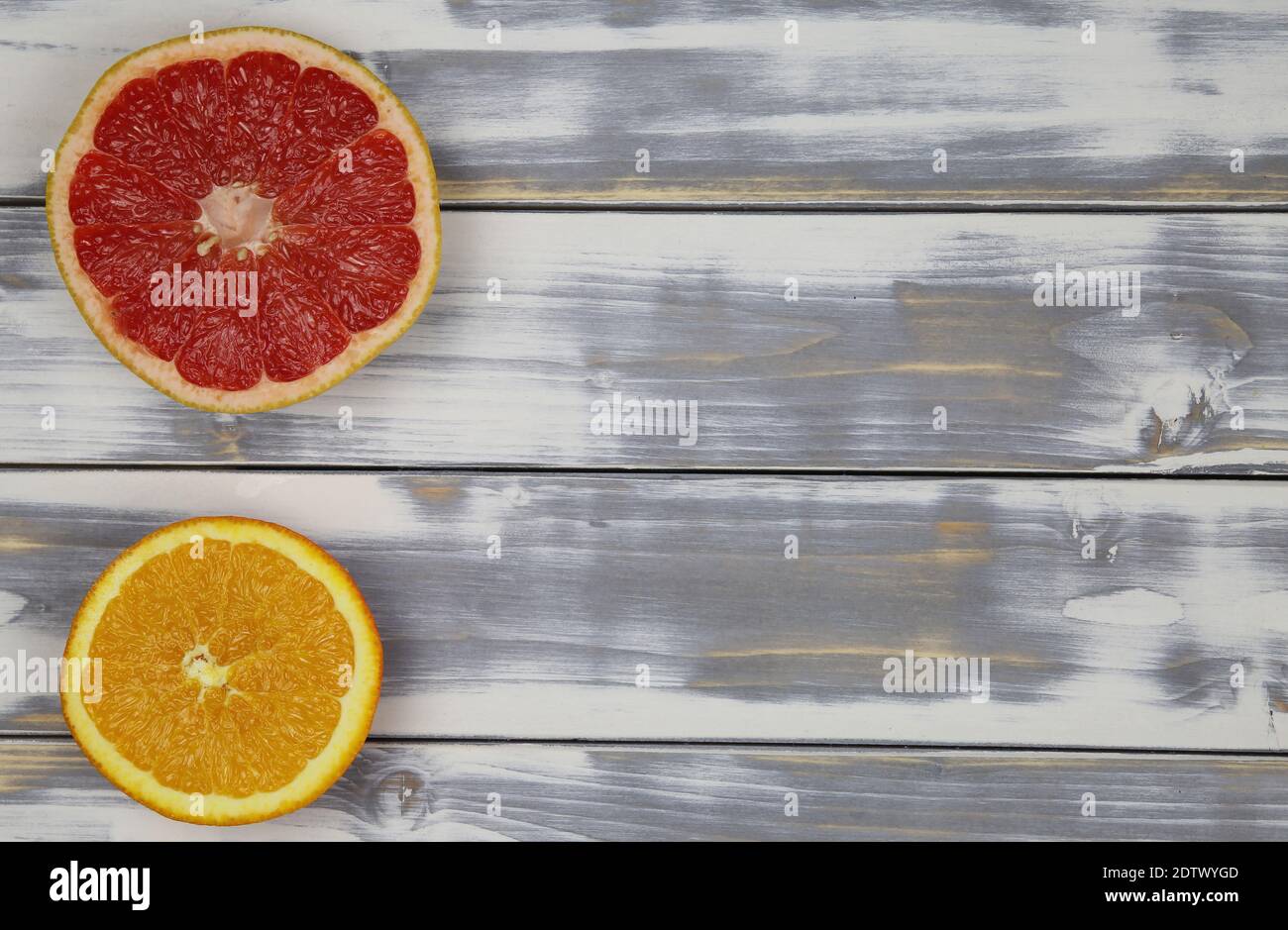Draufsicht auf zwei vereinzelte Obsthälften, rot-reife Grapefruit und Orange, auf weißem Naturholztisch mit Platz für Text Stockfoto