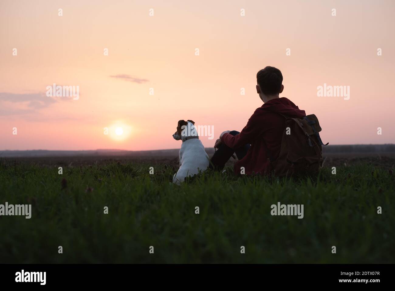 Teenager auf der grünen Wiese mit kleinen weißen Hund. Freundschaft und Travel Concept Stockfoto