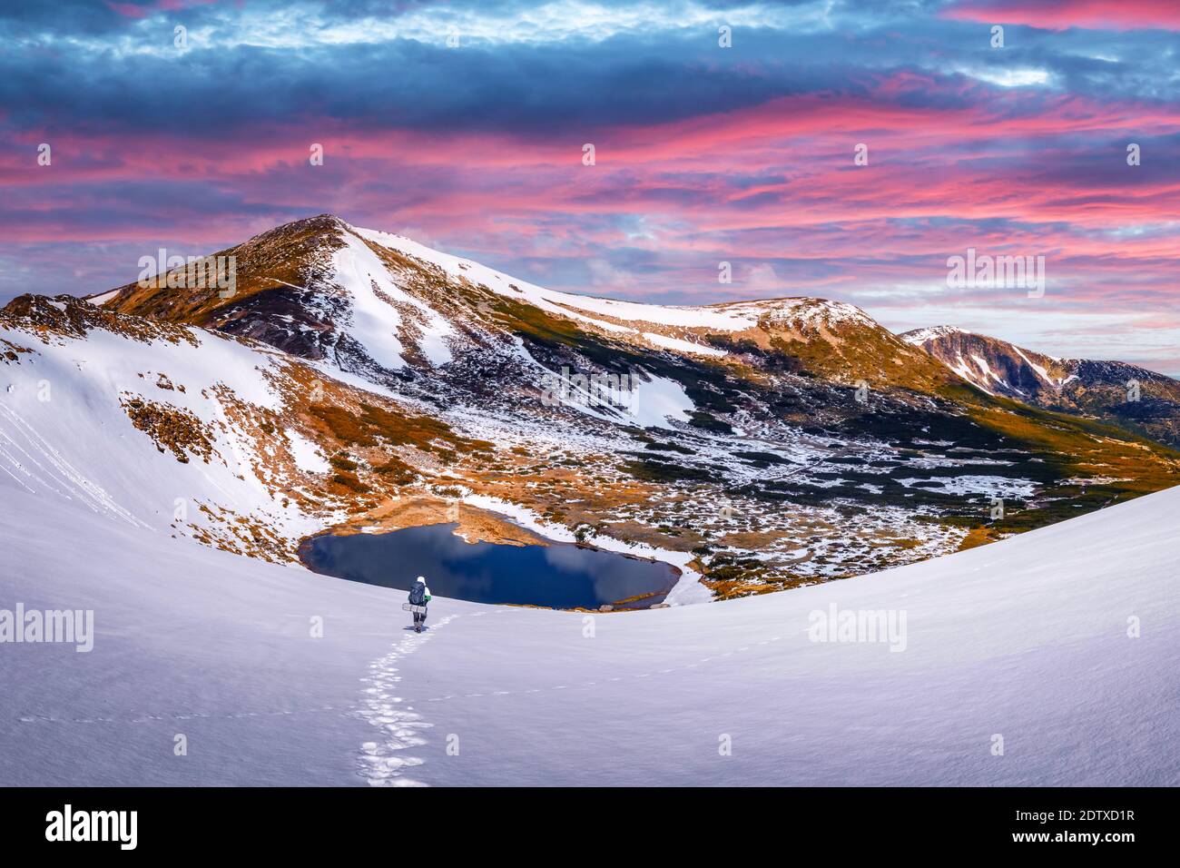 Tourist mit Rucksack Wandern in Frühlingsbergen. Gefrorener See und rosa Sonnenuntergang Himmel auf dem Hintergrund. Landschaftsfotografie Stockfoto