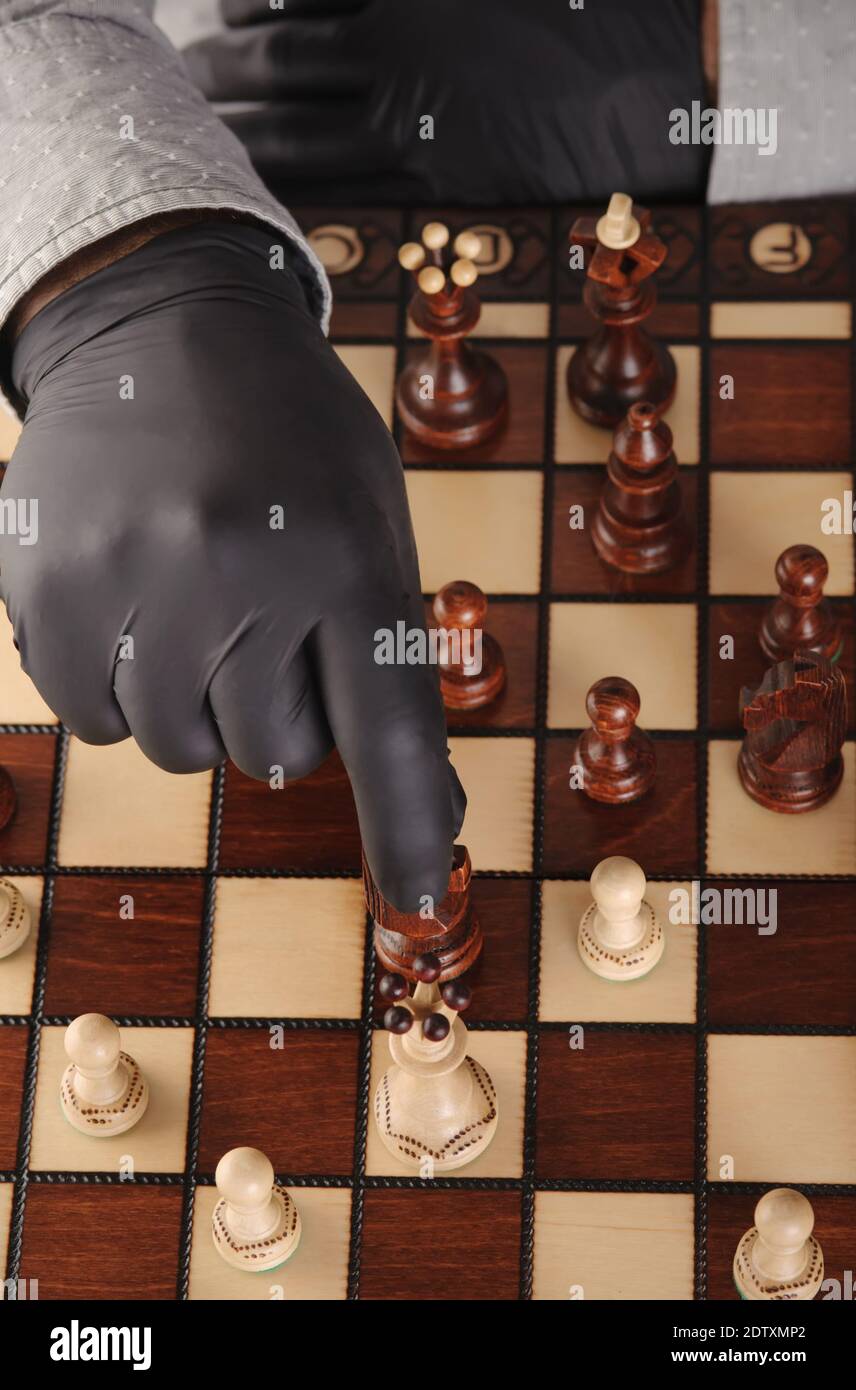 Person in schwarzen Handschuhen und medizinische Maske spielen Schach zu Hause während Quarantäne.Vertikale Ausrichtung. Stockfoto