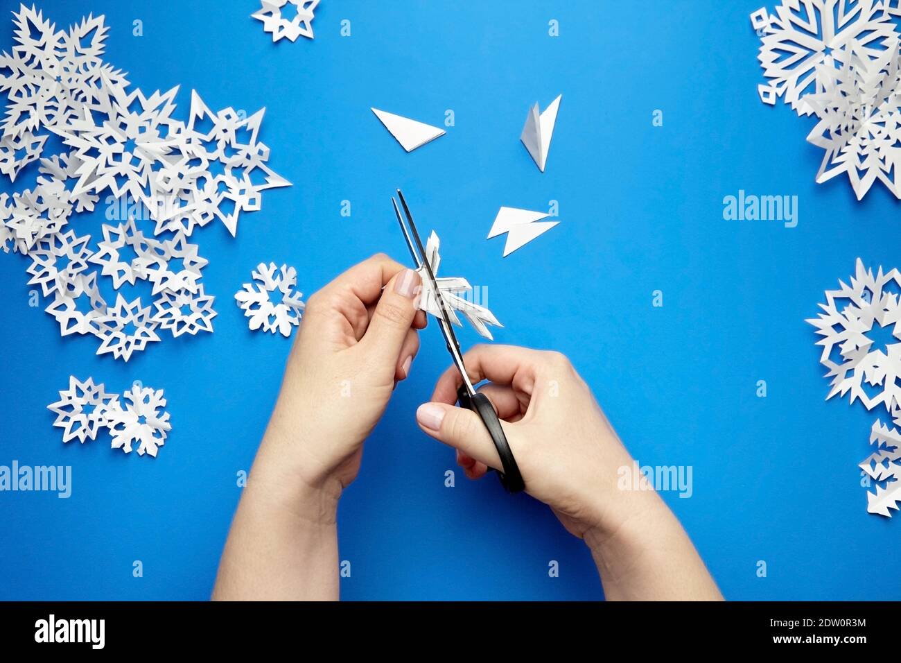 Hände schneiden weißes Papier Schneeflocken auf blauem Hintergrund Stockfoto