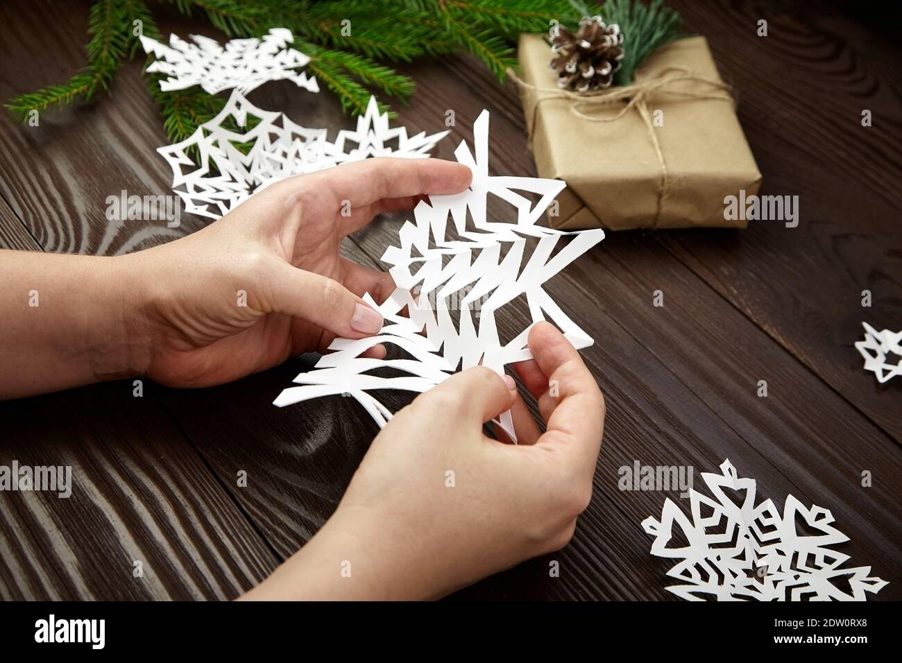 Hände machen weiße Papier Schneeflocke über Holztisch Stockfoto