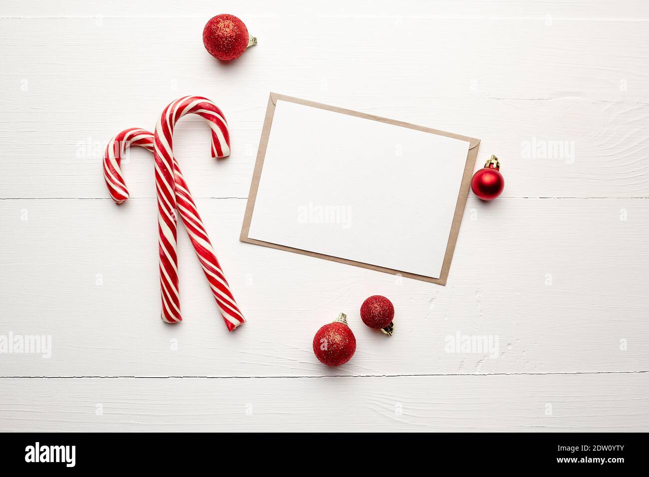 Grußkarte Mockup mit Süßigkeiten Stöcke und roten weihnachtsdekorationen Auf weißem Holzhintergrund Stockfoto