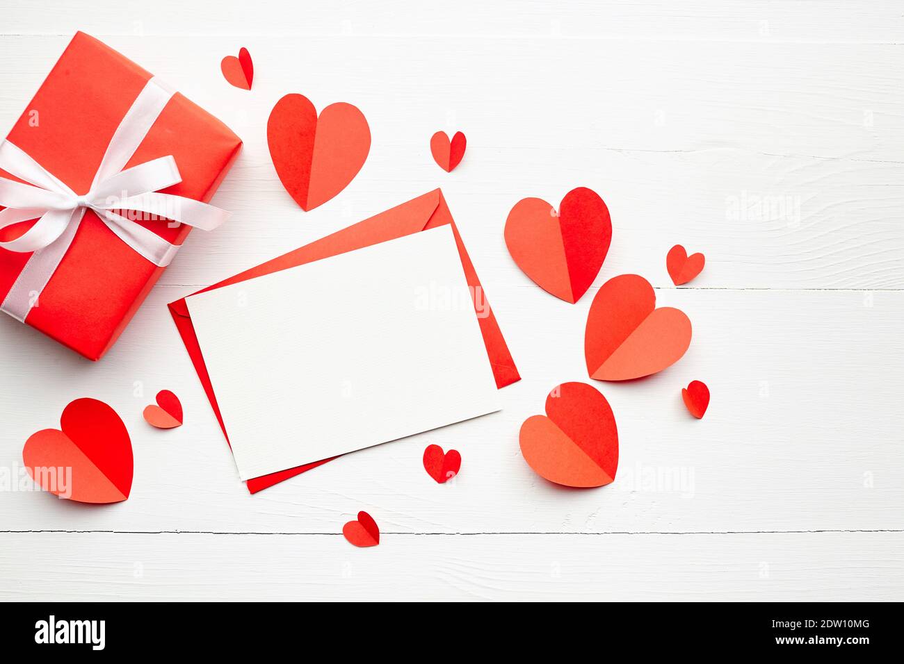 Valentinstag Grußkarte, flach liegend, Draufsicht. Grußkarte mockup, weiße leere Karte mit Umschlag und roten Papierherzen, Geschenkbox mit Band auf Stockfoto