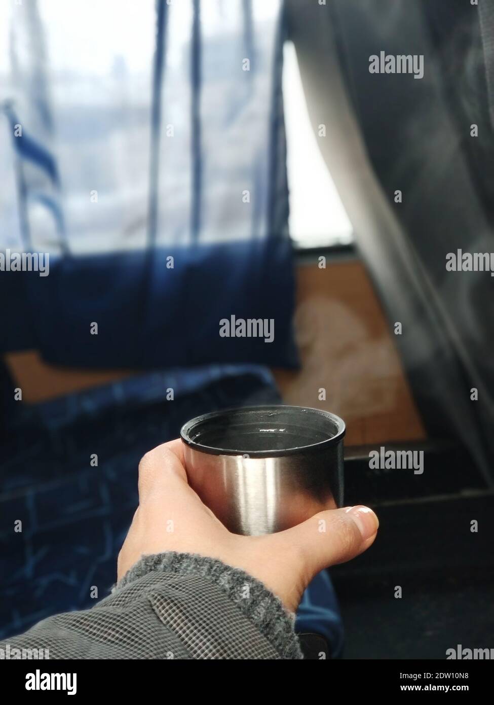 Ein Mann hält in der Hand eine Kappe aus einer Thermoskanne mit dampfendem heißen Tee, in der Kabine des Busses. Heißes Getränk während der Reise. Stockfoto
