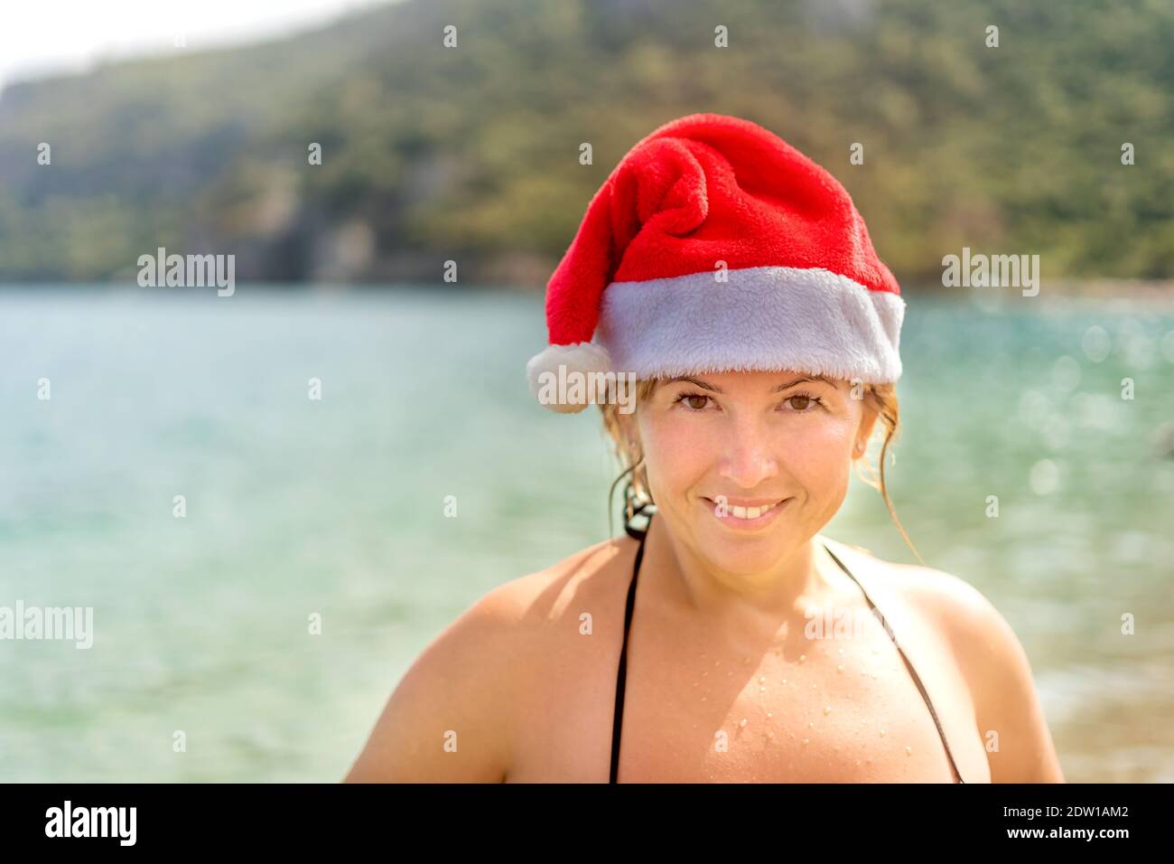 Nahaufnahme einer lächelnden kaukasischen Frau in Badeanzug und Weihnachtsmann Hut am tropischen Strand. Nahaufnahme. Leerzeichen für Text. Stockfoto