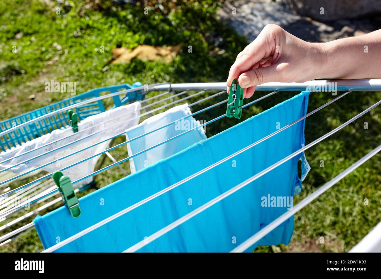 Legt Wäsche auf. Eine Frau hängt nasse Kleidung auf einem Wäscheständer vor dem Hintergrund von Gras Stockfoto