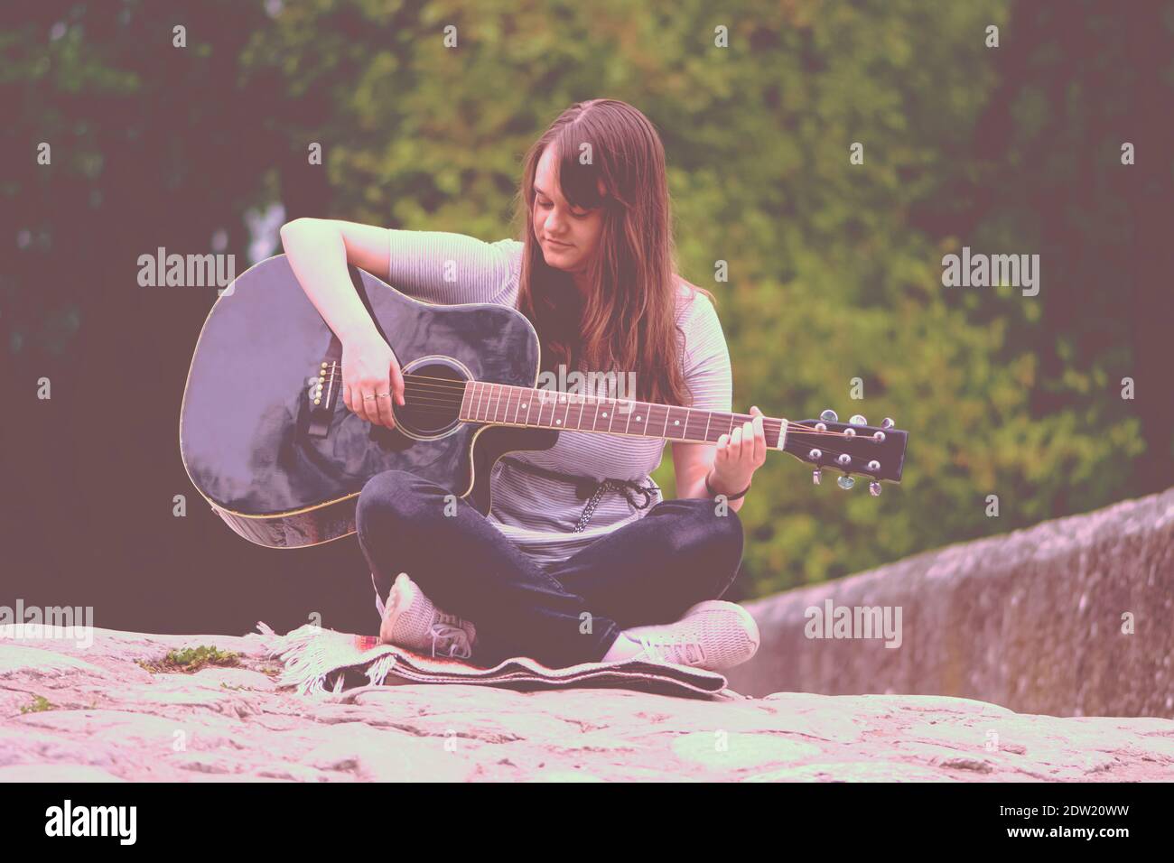 Hübsches Teenager Mädchen Gitarre spielen, während auf der Steinbrücke sitzen Stockfoto
