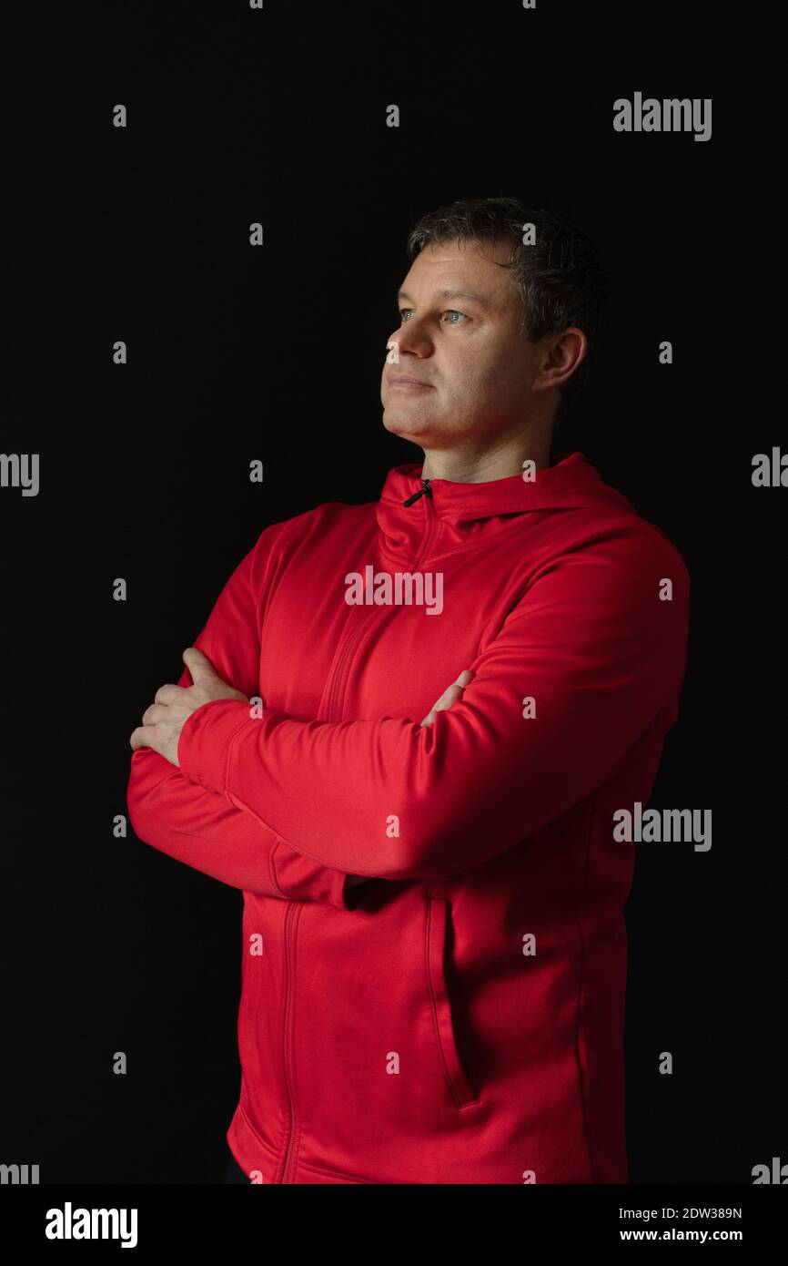 Porträt eines nachdenklichen männlichen Athleten im Alter von 35 bis 45 Jahren in rotem Sportkleid auf schwarzem Hintergrund. Stockfoto