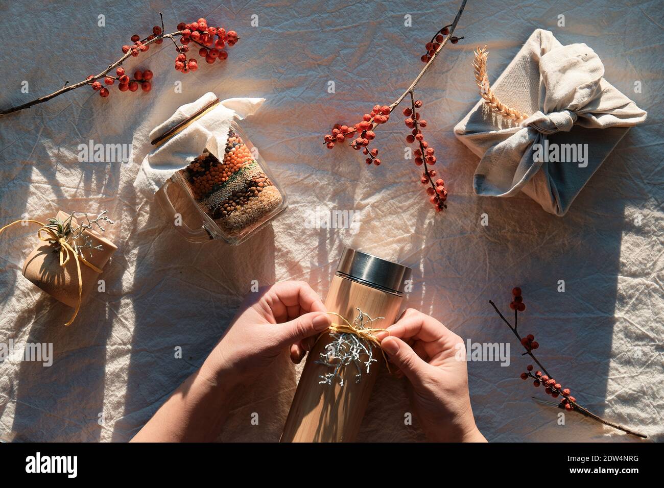 Flat Lay mit Zero Waste Weihnachtsgeschenke. Hände binden Schleife auf isolierte Kolben. Weihnachten Geschenk in Handtuch, Einmachglas mit geschichteten Bohnen verpackt. Nachhaltig Stockfoto