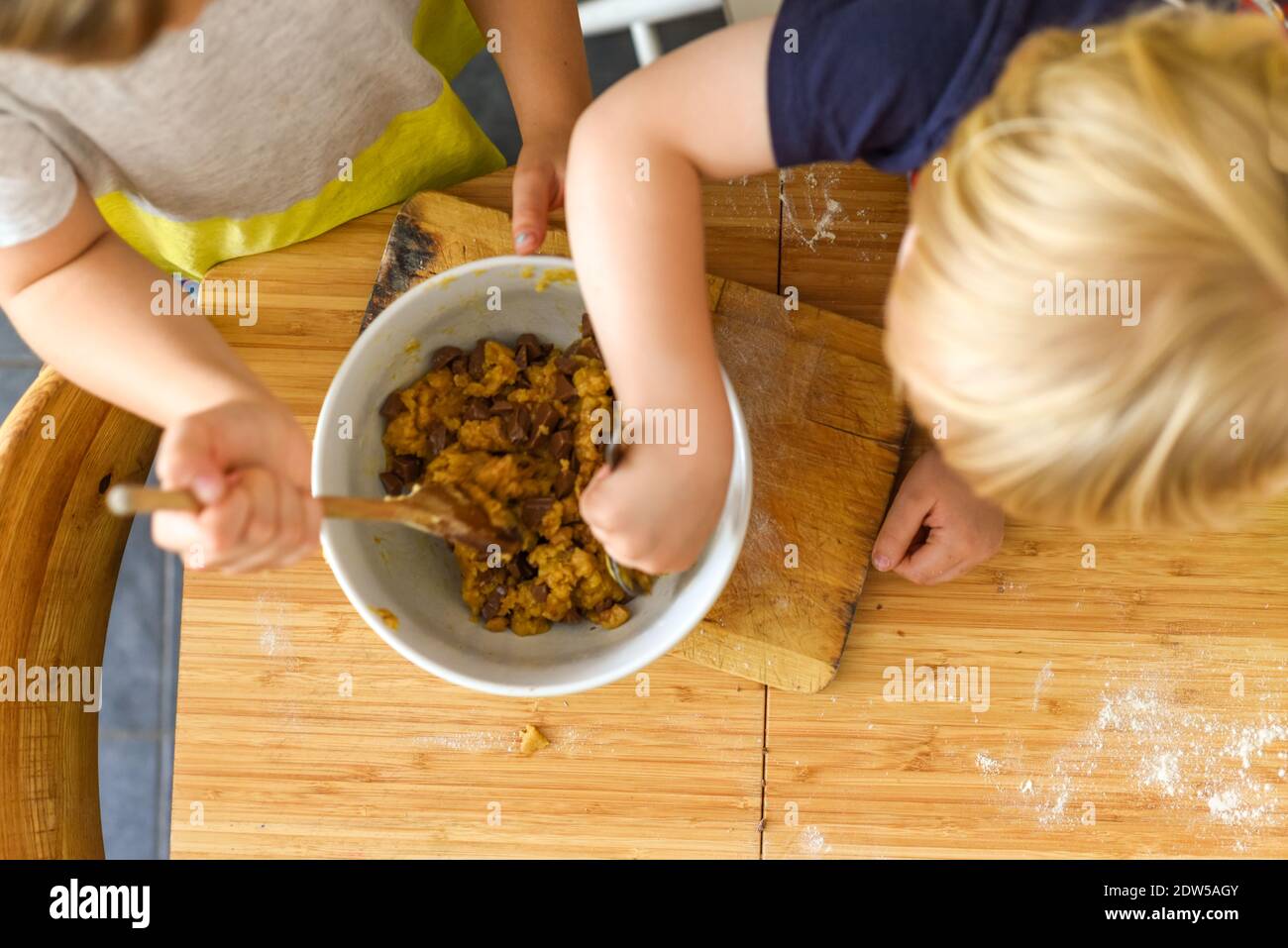 Kinder, die zu Hause auf einem Küchentisch essen Mischen Plätzchenteig Stockfoto