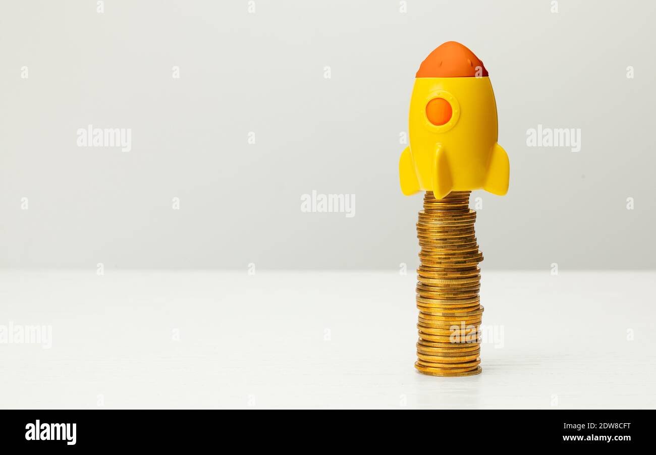 Rakete und Stapel von Goldmünzen auf grauem Hintergrund. Stockfoto