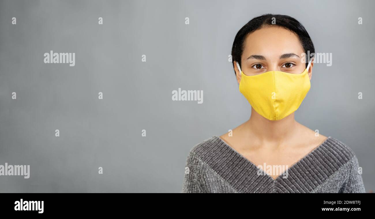 Junge hübsche Frau trägt gelbe Maske und bleibt gegen grau Hintergrund Stockfoto