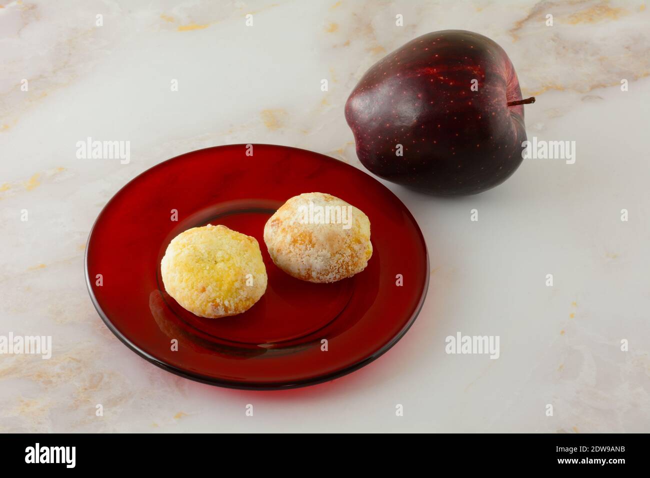 Deutscher Apfelstollen Kuchen Bisse auf roter Glasplatte mit Frischer roher roter köstlicher Apfel auf dem Tisch Stockfoto