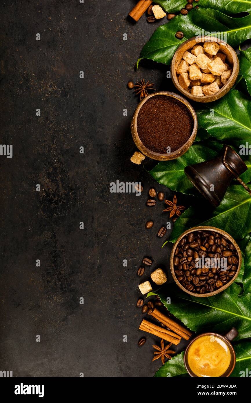 Kreative flach mit gefrästen Kaffee, Kaffeebohnen, brauner Zucker und tropische Blätter auf dunklen rustikalen Hintergrund, Copyspace Stockfoto