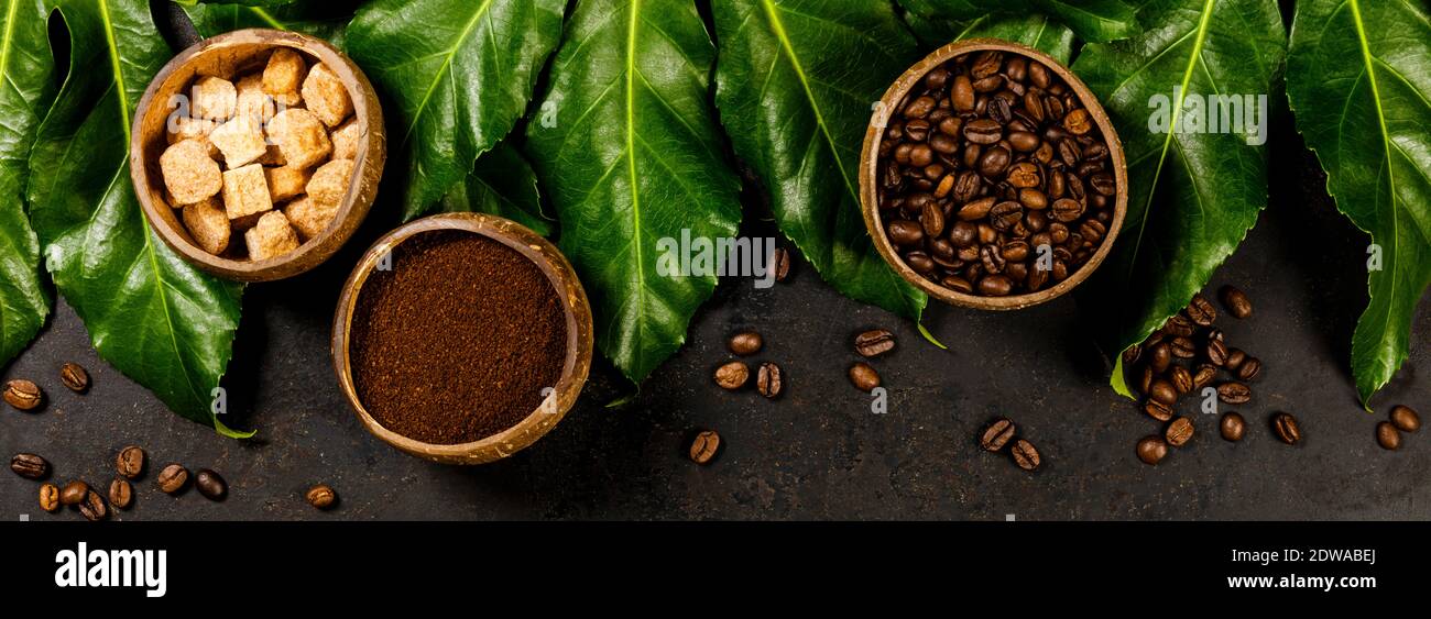 Kreative flach mit gefrästen Kaffee, Kaffeebohnen, brauner Zucker und tropische Blätter auf dunklen rustikalen Hintergrund, Copyspace Stockfoto