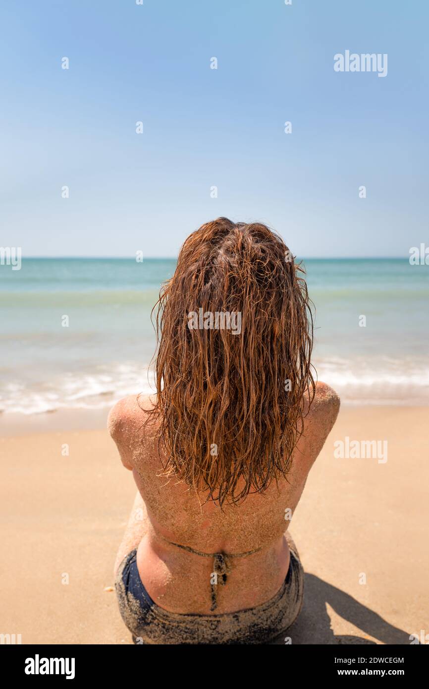 Frau, die auf ihrem Rücken im Sand sitzt und anschaut Das Meer Stockfoto