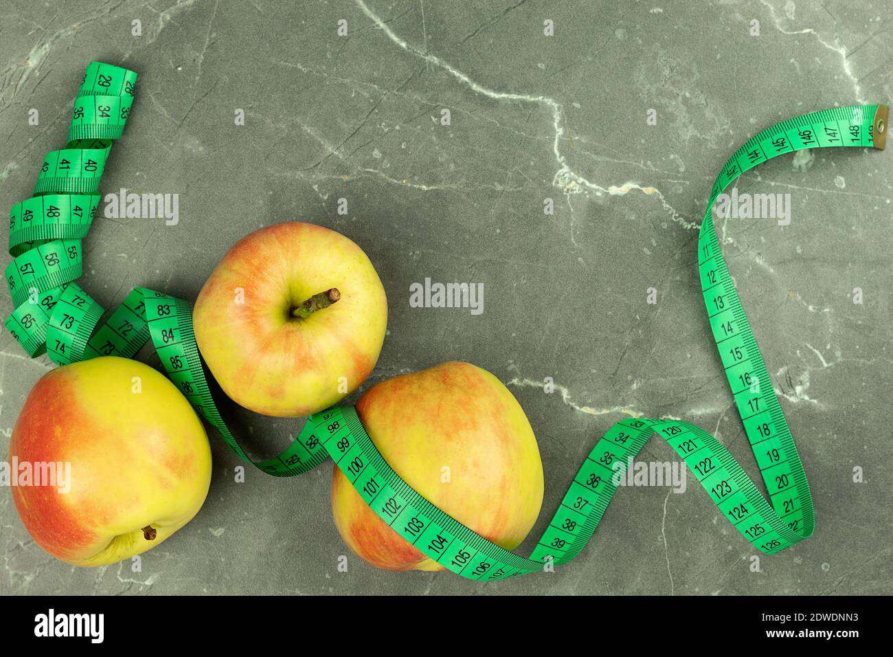 Äpfel und Meter auf grauem Hintergrund. Hintergrund mit Platz für Text zum Thema Ernährung, Gewichtsverlust, Sport, Vegetarismus, gesunde Ernährung Stockfoto