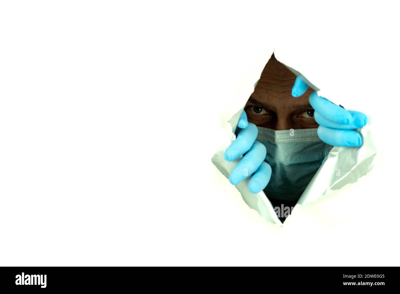 Ein Mann mit Maske und Handschuhen schaut durch das Loch. Situation ein Mann in einer medizinischen Maske guckt durch ein Loch in die Wand Stockfoto