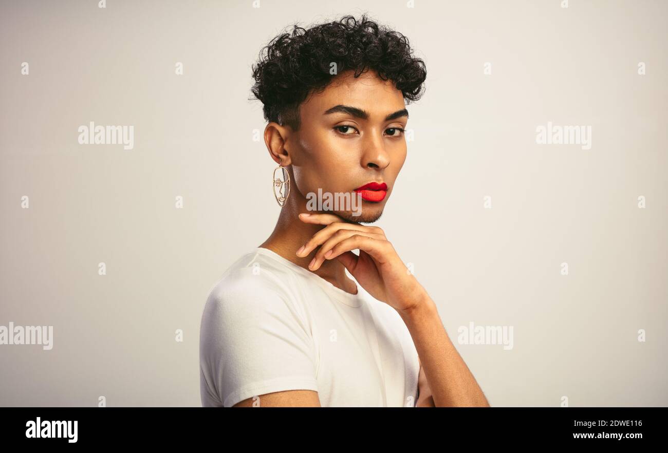 Portrait von einem schönen Gay Mann mit Make-up. Transgender männlich mit rotem Lippenstift und Ohrring Blick auf die Kamera. Stockfoto