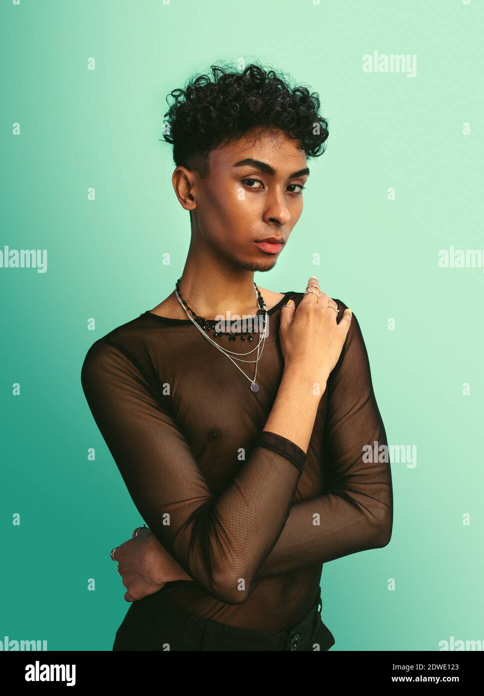 Androgynen Mann in schwarzem Mesh-T-Shirt. Transgender Mann posiert vor blauem Hintergrund. Stockfoto