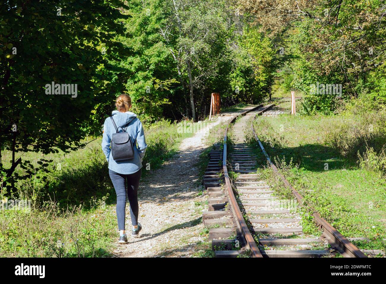 Rückansicht eines jungen Wandertouristin Mädchen genießen erstaunliche Schönheit der Natur. Ausflug auf alte schmale Eisenbahn im Wald. Stockfoto
