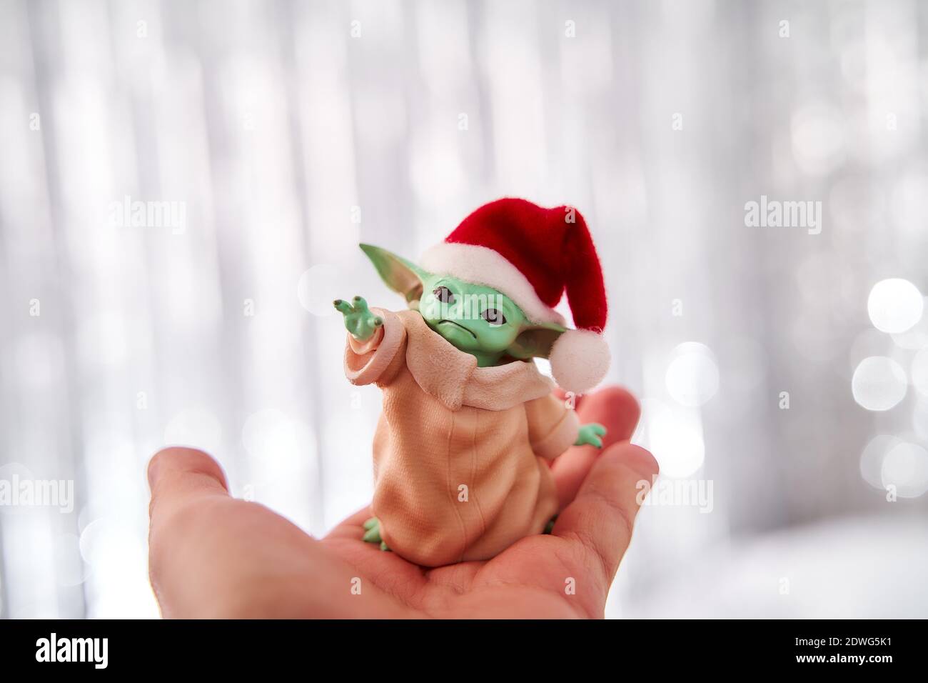 Dez, 2020: Darstellung von Baby Yoda, einer Action-Figur, die in einer roten Mütze auf weihnachtlichem Hintergrund steht. Bokeh-Effekt. Stockfoto