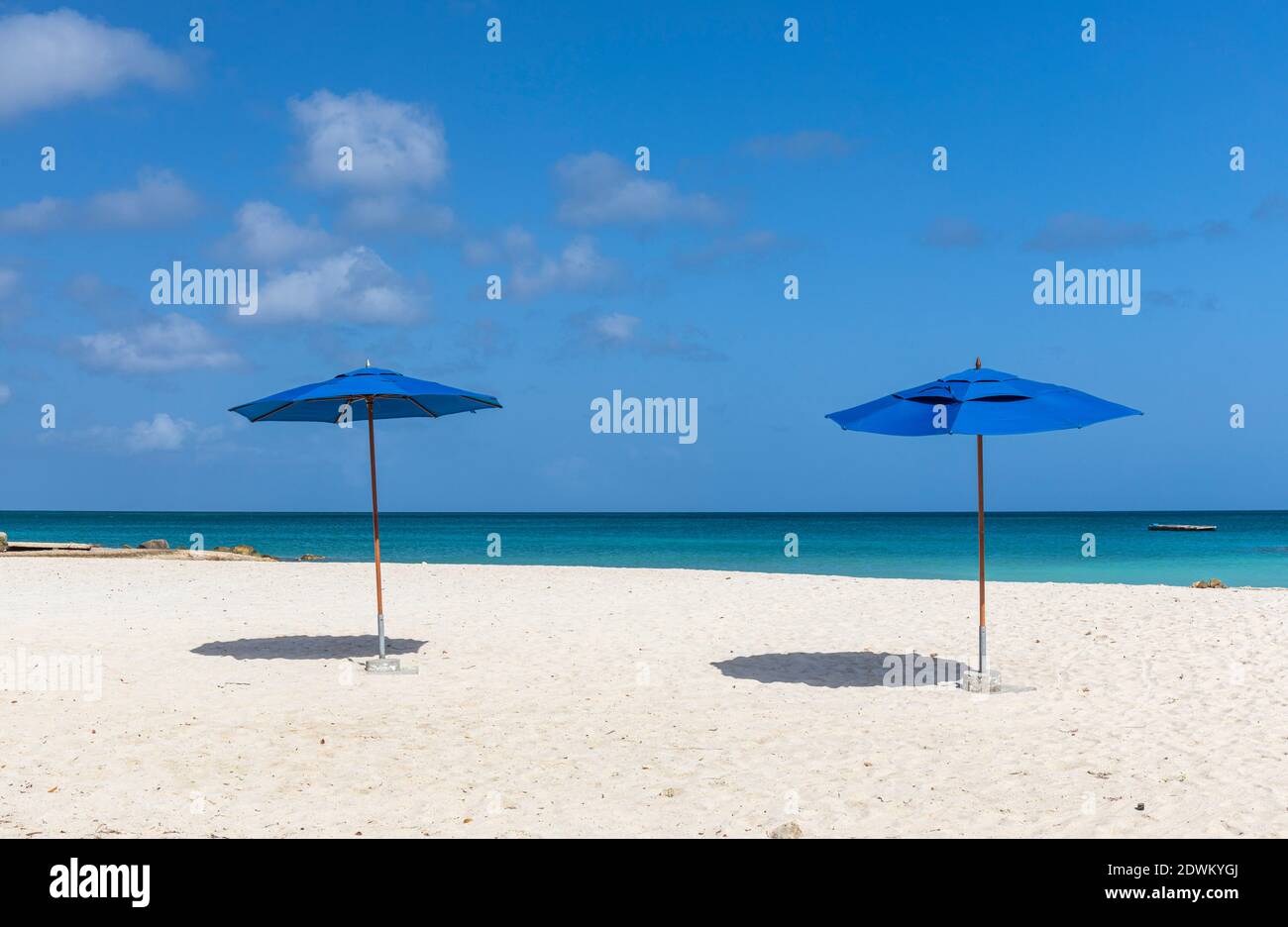 Zwei blaue Sonnenschirme (Sonnenschirme) an einem karibischen weißen Sandstrand mit türkisfarbenem Meer und blauem Himmel. Palm Beach Aruba, karibische Insel Stockfoto