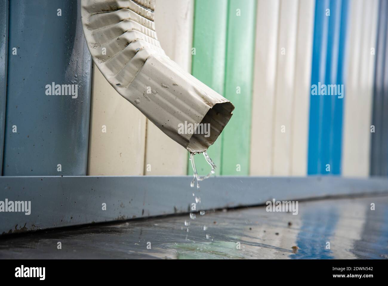 Regenwasser fließt über einen Abfluss vom Dach des Gebäudes. Entfernung von Regenwasser. Downpipe Weiß Stockfoto