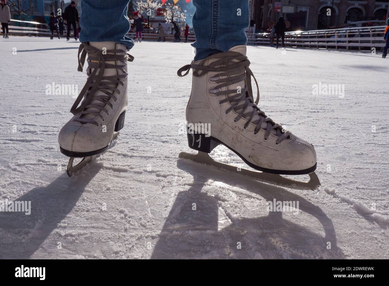 Füße in Schlittschuhe. Öffentliche Eislaufbahn, zwei Schlittschuhe, zerkratztes Eis, sonniger Tag im Winter. Mädchen Schlittschuhlaufen auf der Eisbahn. Nahaufnahme. Stockfoto