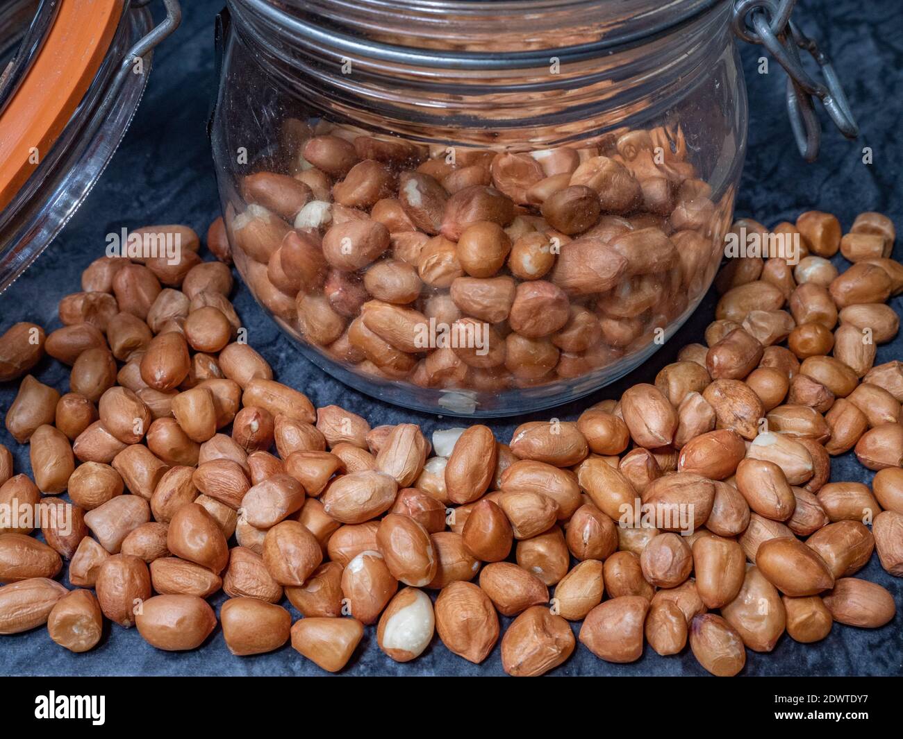 Nahaufnahme von rohen Erdnüssen (mit Samenbeschichtungen / Schalen intakt), innen und um ein Glas Vorratsglas, mit einem Metallverschluss und luftdichtem, gummiversiegeltem Deckel. Stockfoto