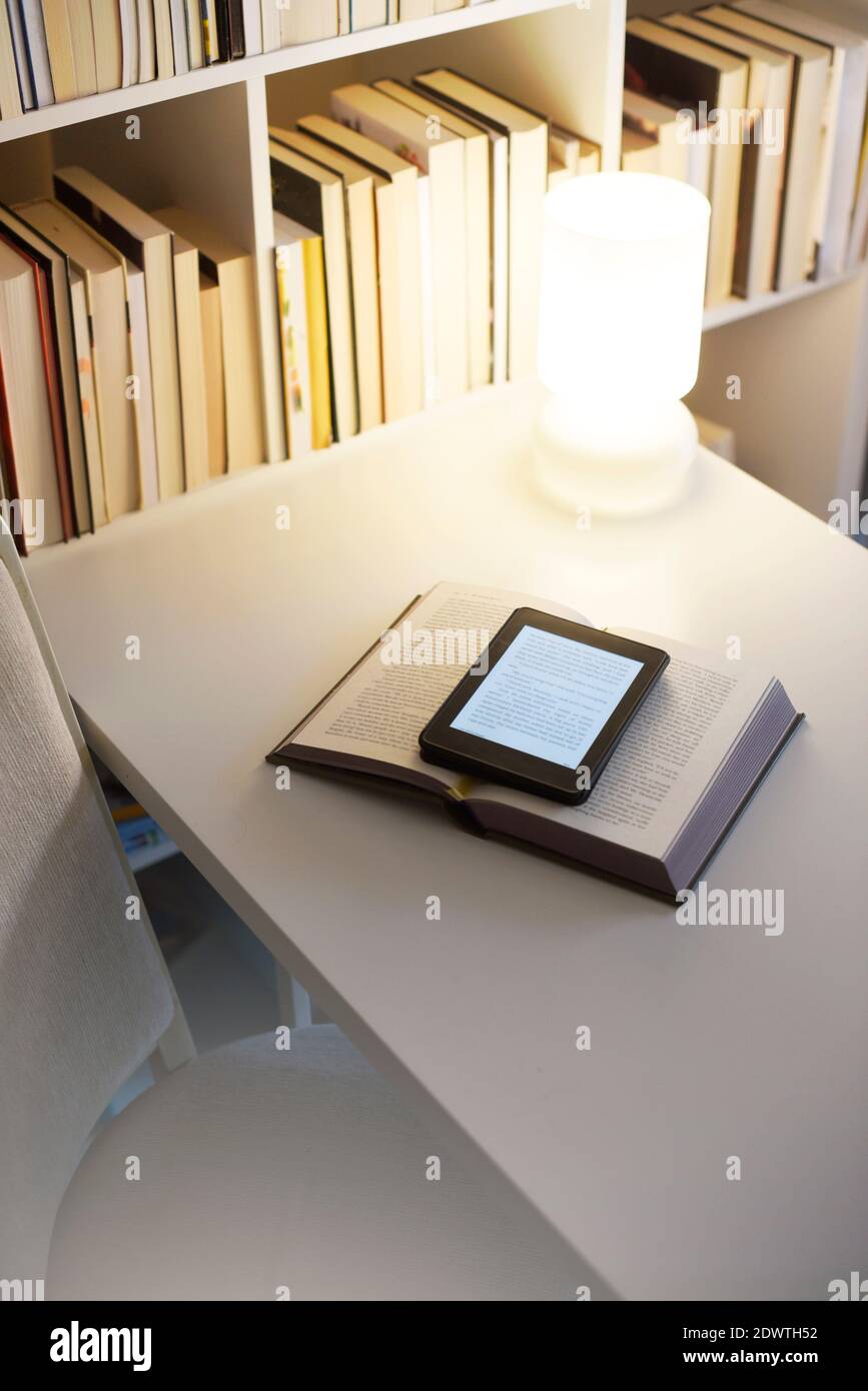 Digitale und physische Bücher auf dem Tisch. Moderne Lektüre in einem weißen minimalistischen Setting. Von zu Hause aus lernen Stockfoto