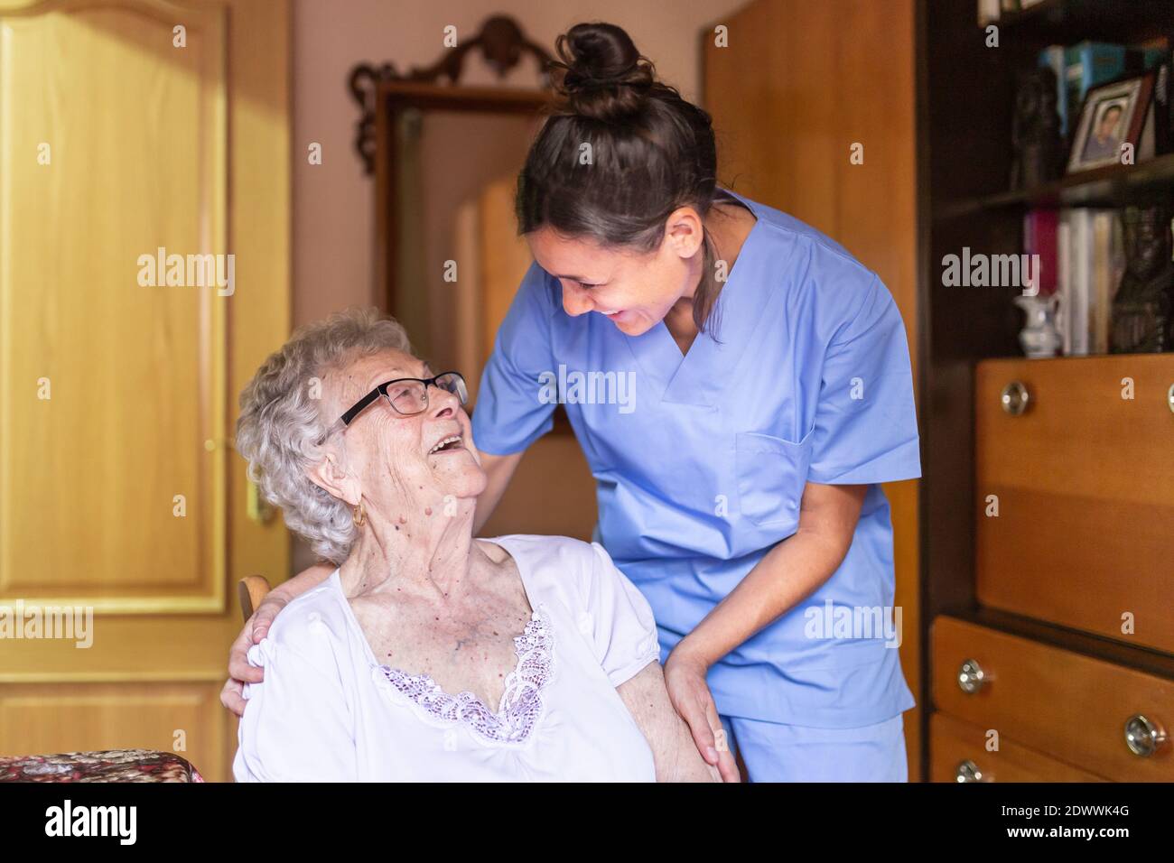 Glückliche ältere Frau, die mit ihrem Betreuer zu Hause lacht. Pflegekonzept für Senioren. Stockfoto