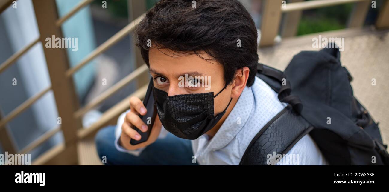 Portrait eines jungen Mannes mit Maske, sitzt er auf der Essstappe und telefoniert. Stockfoto