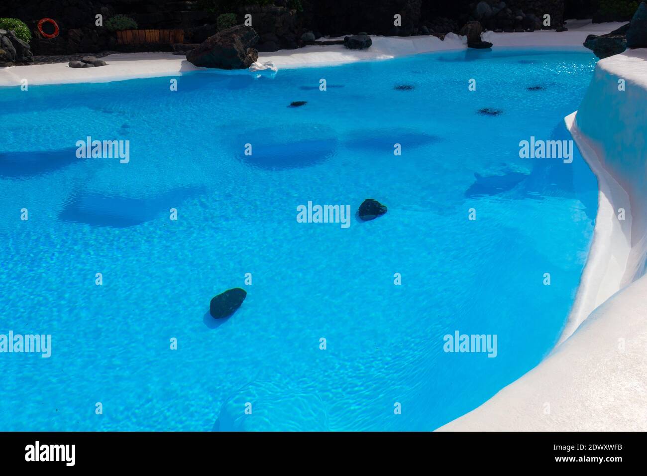 Intensiver blauer Swimmingpool mit vulkanischem Gestein auf dem Boden bei Lanzarote Wahrzeichen. Touristenattraktion, Integration der Natur in Architekturkonzepte Stockfoto