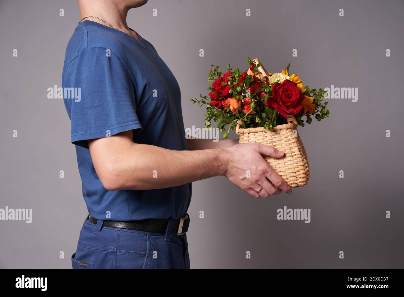 Ein weißer Mann in einem blauen T-Shirt hält einen Blumenkorb mit einem Kopierplatz auf einem grauen Hintergrund aus, Blumenlieferung Stockfoto