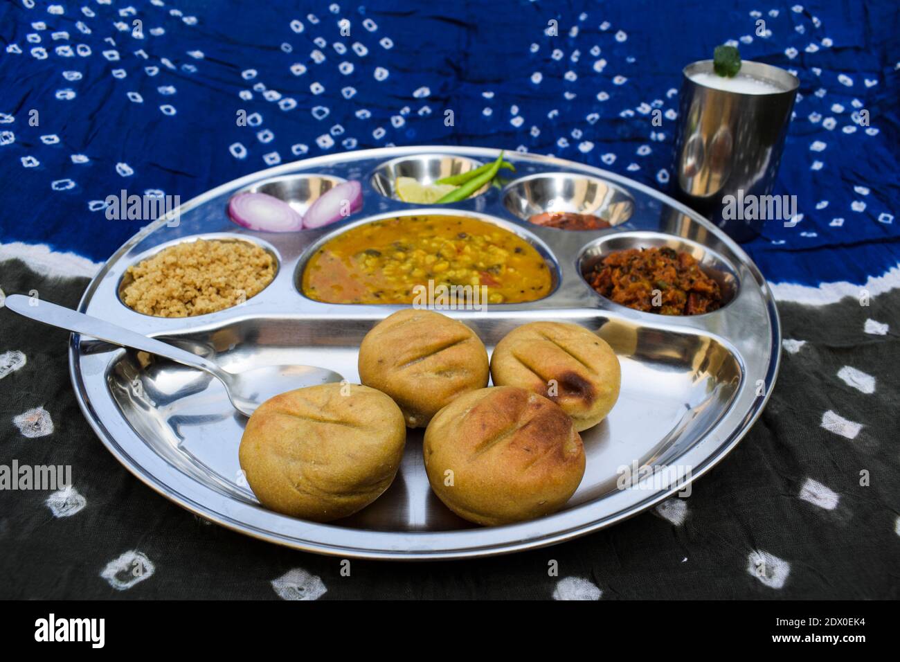 Beliebte Rajasthani Essen Dal bati serviert mit Salaten, Tomate Chutney, Knoblauch Chutney und Glas Buttermilch mit Hintergrund der traditionellen Stoff Krawatte ein Stockfoto